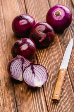 cut and whole red onion near knife on wooden table clipart