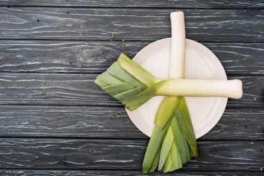 top view of fresh green leek on plate on wooden surface clipart
