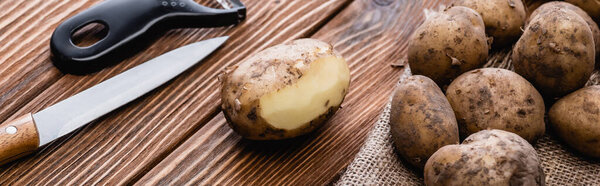 dirty potatoes on wooden table with peeler and knife, panoramic shot