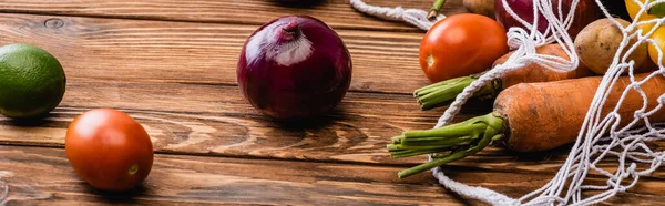 fresh ripe vegetables scattered from string bag on wooden table, panoramic shot