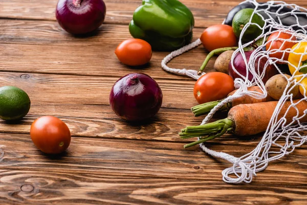 fresh ripe vegetables scattered from string bag on wooden table
