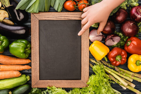 cropped view of person pointing at empty chalkboard near fresh colorful vegetables