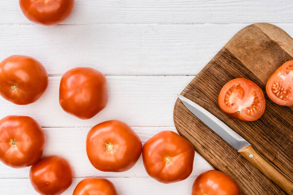 top view of ripe tomatoes on chopping board with knife on white wooden table