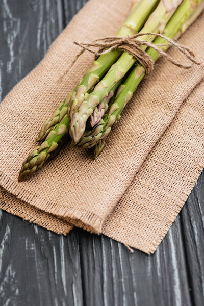 bundle of fresh green asparagus on burlap on wooden surface