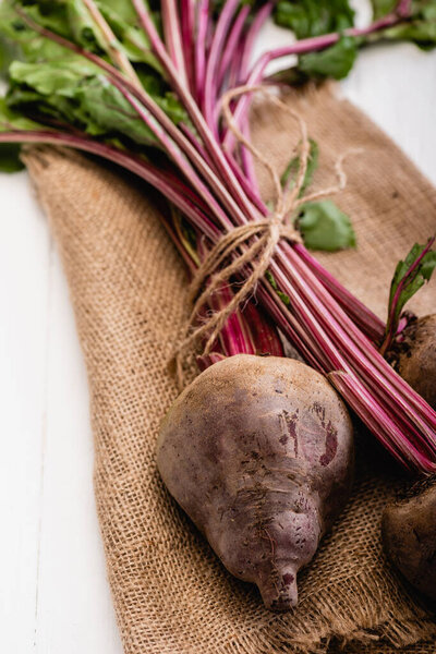 close up view of beetroot tied with rope on sackcloth on white wooden table