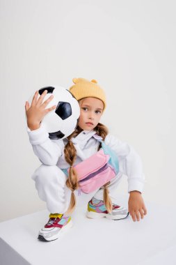 blonde girl in sportswear posing with soccer ball on cube isolated on white clipart