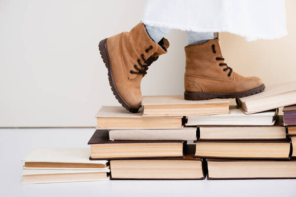 cropped view of girl in brown boots walking on vintage books