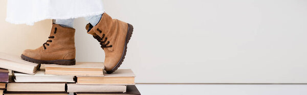 cropped view of girl in brown boots walking on vintage books, panoramic shot