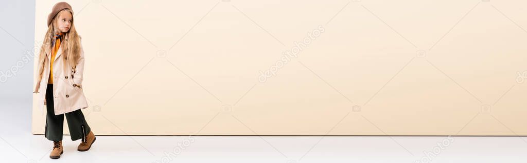 fashionable blonde girl in autumn outfit walking on beige and white background, panoramic shot