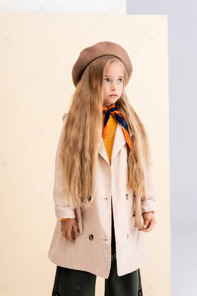fashionable blonde girl in autumn outfit looking away on beige and white background