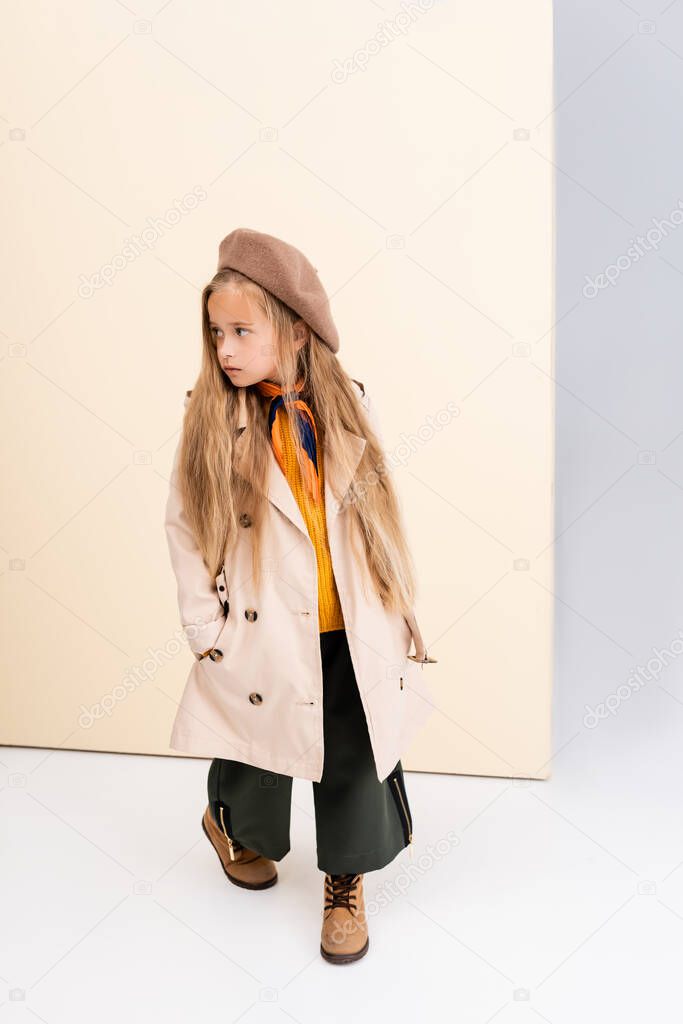 fashionable blonde girl in autumn outfit walking on beige and white background