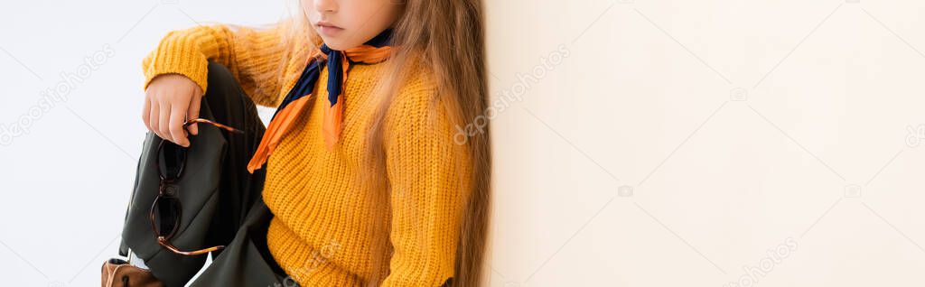 cropped view of fashionable blonde girl in autumn outfit with sunglasses on beige and white background, panoramic shot