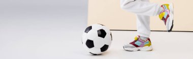 cropped view of girl in sneakers posing with soccer ball on beige and white background, panoramic shot clipart