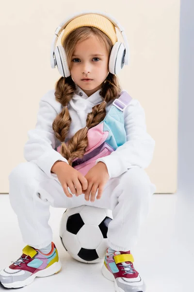 Blondynka Dziewczyna Strój Sportowy Słuchawki Pozowanie Piłką Nożną Beżowym Białym — Zdjęcie stockowe