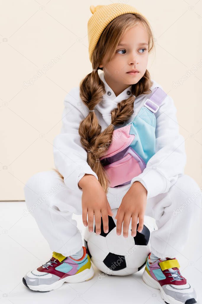 blonde girl in sportswear posing with soccer ball on beige and white background