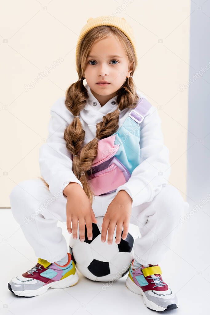 blonde girl in sportswear posing with soccer ball on beige and white background