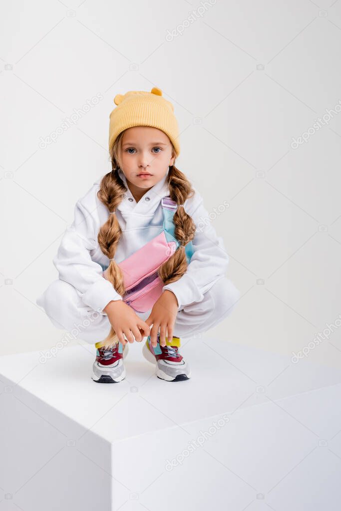 blonde girl in sportswear sitting on cube isolated on white