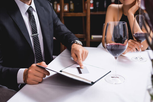 Обрезанный вид человека положить кредитную карту в счет ресторана возле бокалов вина и подруги 