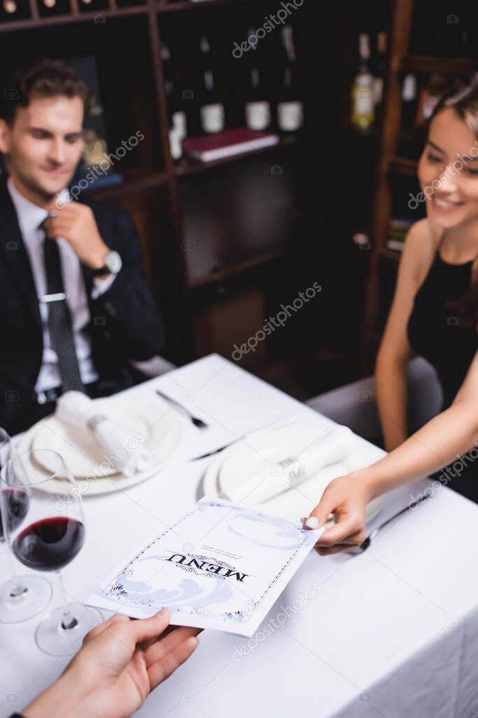 Selective focus of waiters giving menu to woman at table in restaurant