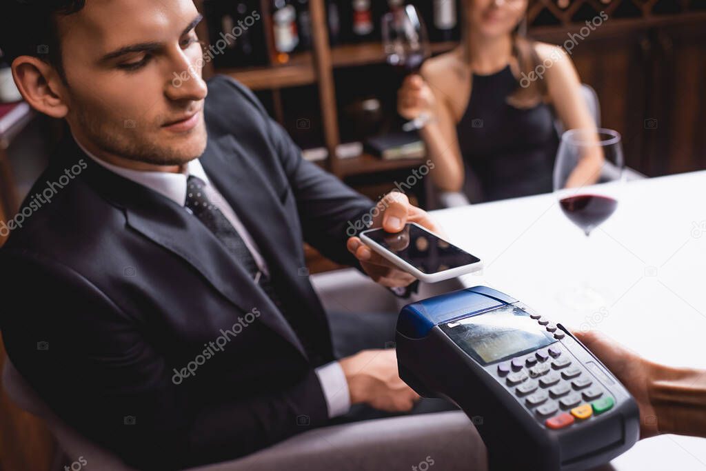 Selective focus of man paying with smartphone near waitress with payment terminal during dating in restaurant 