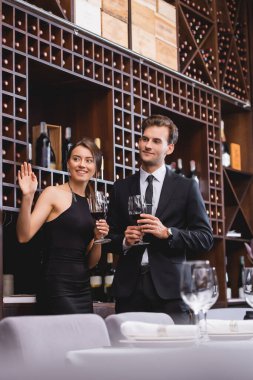 Seçici odak noktası, restoranda erkek arkadaşının yanında bir kadeh şarap içerken zarif bir kadının el sallaması. 