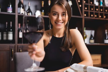 Seçici odak noktası, elinde şarap kadehi olan ve restoranda kameraya bakan genç bir kadın. 