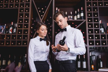 Şarap garsonları restoranda rafın yanında şarap şişesine bakıyorlar. 