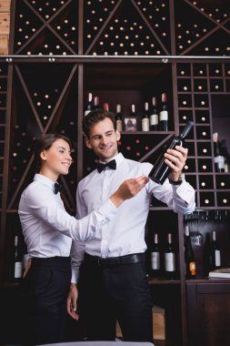 Şarap garsonunun seçici odağı elinle restorandaki meslektaşının yanındaki şarap şişesini işaret ediyor. 