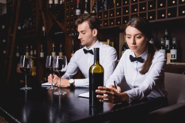 Şarap garsonlarının seçici odak noktası şişenin yanındaki defterlere ve restorandaki şarap kadehlerine dikkat çekmek.