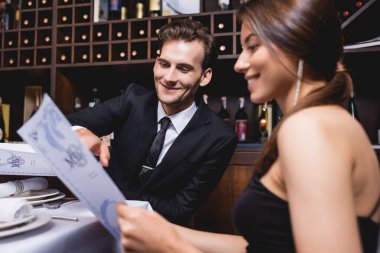 Resmi giyinen erkeğin seçici odak noktası restoranda şık bir kız arkadaşın yanındaki menüye bakması. 