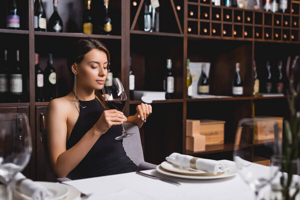 Selective focus of elegant woman holding glass of wine in restaurant 