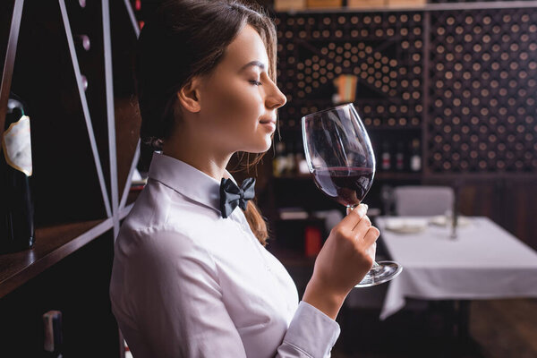 Side view of young sommelier smelling wine in glass with closed eyes 