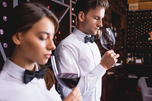 Selective focus of sommelier smelling wine in glass near colleague in restaurant