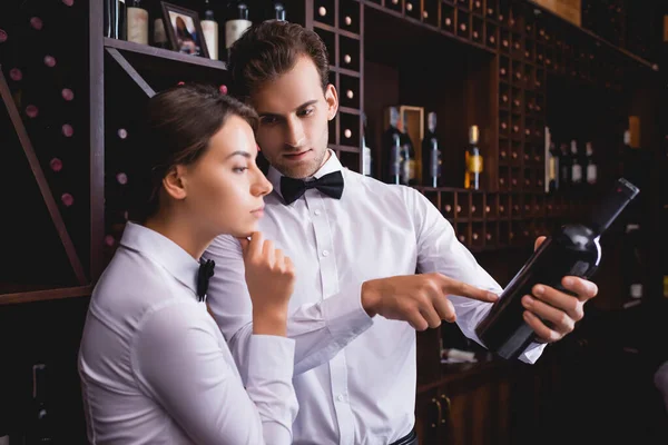 Selective Focus Sommelier Pointing Bottle Wine Thoughtful Colleague Restaurant — Stock Photo, Image