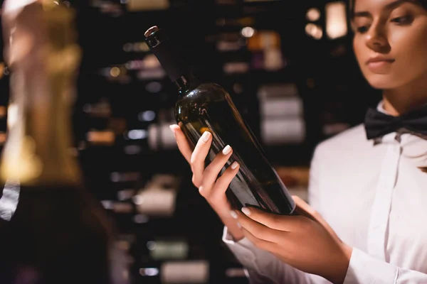 Selective focus of sommelier in shirt and bow tie holding bottle of wine