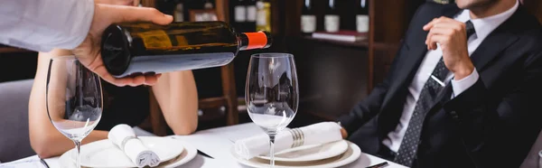 Website header of sommelier pouring wine in glass near couple in restaurant