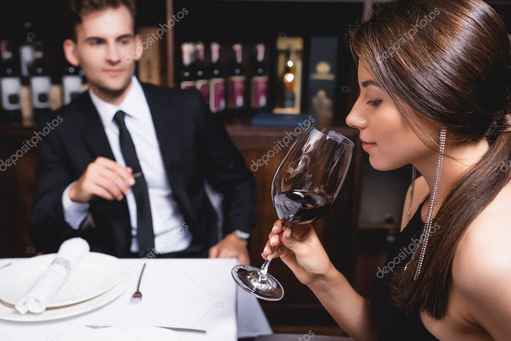 Selective focus of young woman holding glass of wine near boyfriend in restaurant 