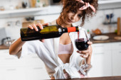 selektiver Fokus der lockigen Frau, die Flasche hält und Rotwein ins Glas gießt