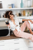 selektivní zaměření ženy držící sklenici červeného vína při sezení na dřevěném povrchu v kuchyni 