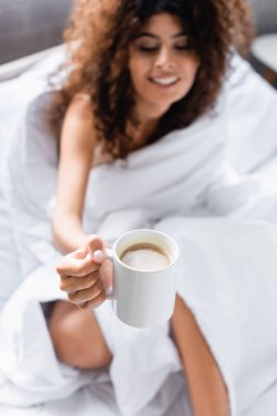 Kıvırcık kadının seçici odağı sabahları bir fincan kahveye bakıyor. 