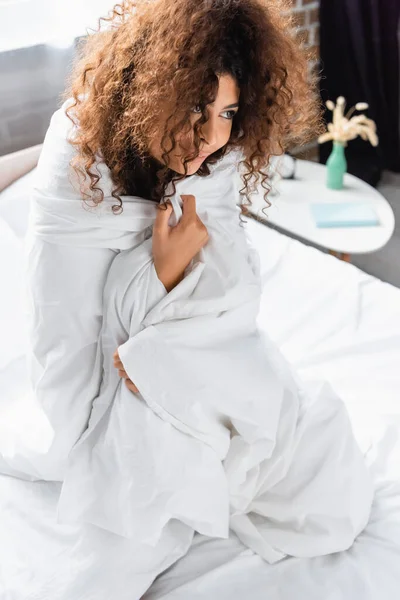 young curly woman wrapped in white blanket looking away