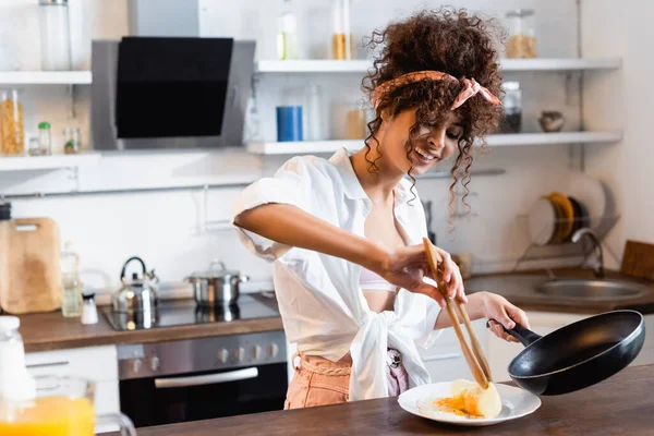 Mulher Encaracolado Alegre Segurando Frigideira Pinças Cozinha Enquanto Serve Ovos — Fotografia de Stock