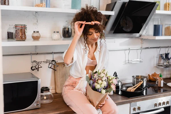 Jeune Femme Bouclée Assise Sur Table Cuisine Regardant Les Fleurs — Photo