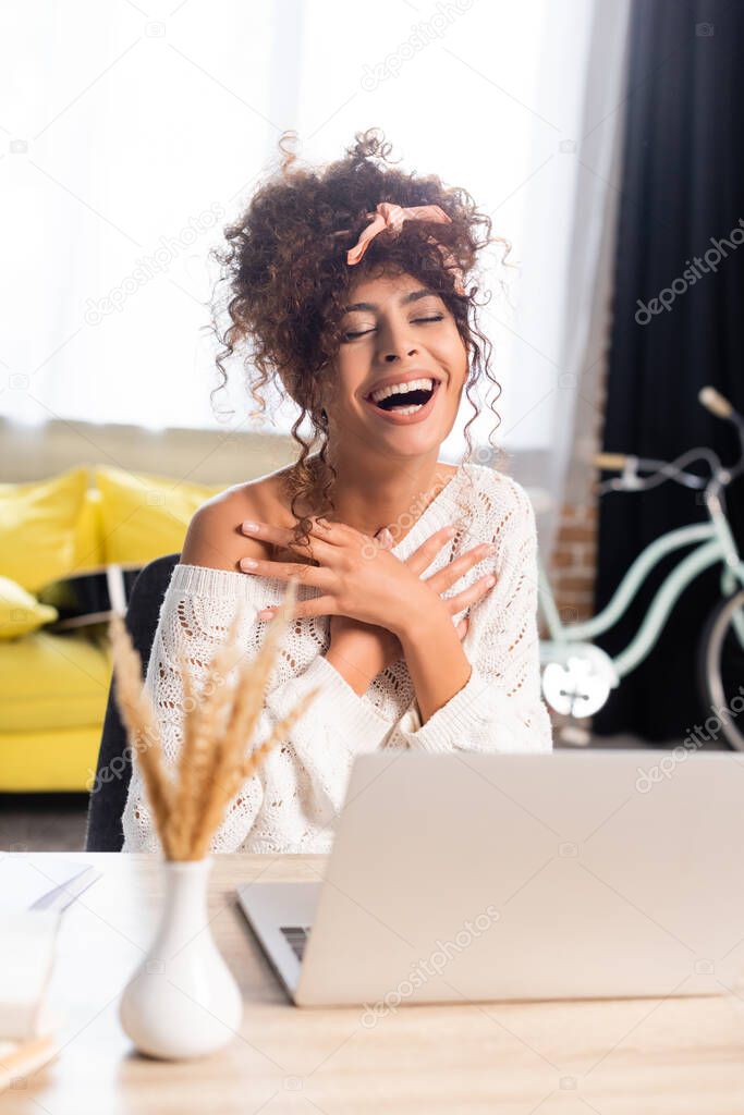 joyful woman with closed eyes laughing near laptop