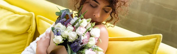 居間で花束を持って花の匂いを嗅ぐ若い女性のパノラマ作物 — ストック写真