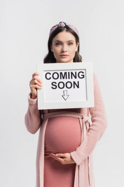 pregnant woman holding board with coming soon lettering isolated on white clipart