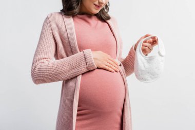 Hamile bir kadının küçük bebek önlüğünü tutarken görüntüsü beyazın üzerinde izole edilmiş.