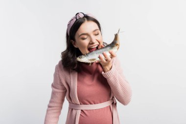 pregnant woman with open mouth and closed eyes holding dried fish isolated on white clipart