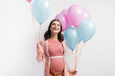 Neşeli ve hamile bir kadın balon tutuyor ve beyazlar içinde yalnız başına yukarı bakıyor.
