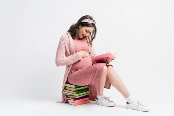 Podekscytowana Ciężarna Kobieta Siedząca Książkach Dotykająca Brzucha Białym — Zdjęcie stockowe